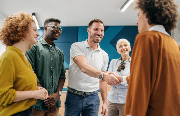 Diverse groupe cheerfully smile while a man facing a woman shakes her hand